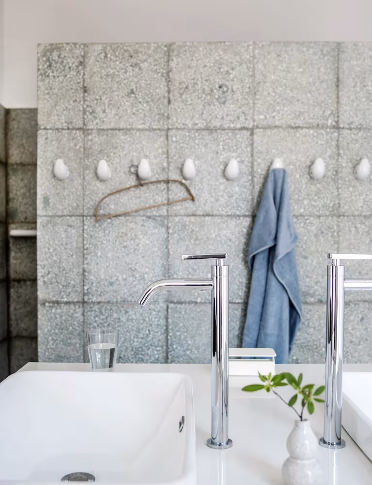 Baño con muro de losas de granito, grifería cromada y lavabo blanco en el Studio Cottage de Clou Architects