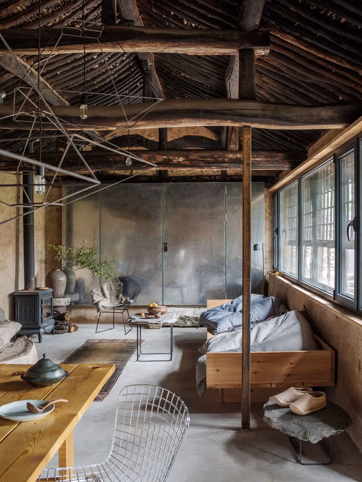Salón del Studio Cottage con estructura de troncos vista, suelo de cemento y ventanas de carpintería oscura, Pekín