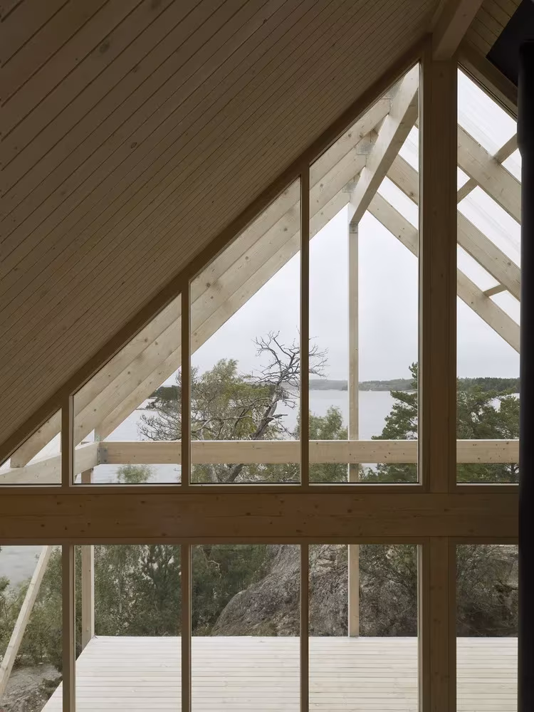 Gran ventana en el hastial de la cabaña de Viggsö con cerchas de madera y vistas al bosque, Arrhov Frick