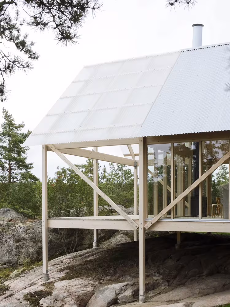 Cabaña de Viggsö sobre pilotes de madera con porche y cubierta translúcida entre pinos, Arrhov Frick Arkitektkontor