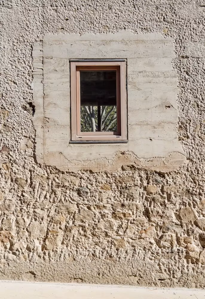 Detalle de la ventana de madera enmarcada en el viejo muro de piedra de la Casa 1413 de H Arquitectes