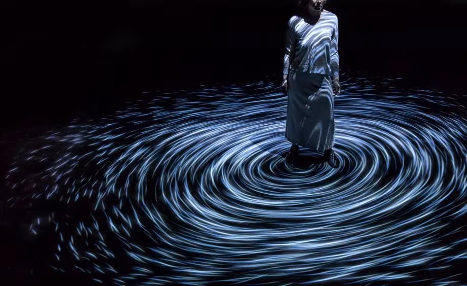 Visitante en el centro de un vórtice luminoso de teamLab que gira a su alrededor sobre el suelo negro
