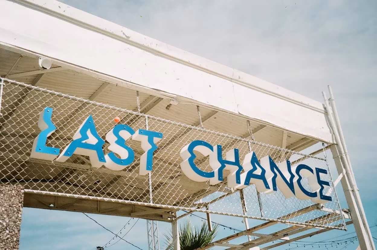 Letrero escultórico «Last Chance» de Wheatley y Dean con letras azules deformadas sobre una marquesina