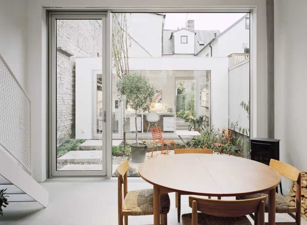 Comedor con mesa redonda abierto por un gran ventanal al patio de la Townhouse de Elding Oscarson, Landskrona