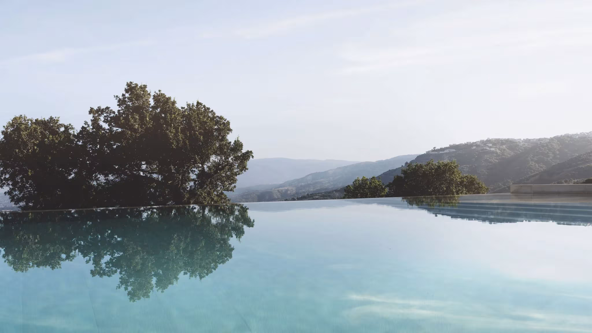Piscina infinita que se funde con un embalse rodeado de montañas, en la selección de piscinas de ÁBATON