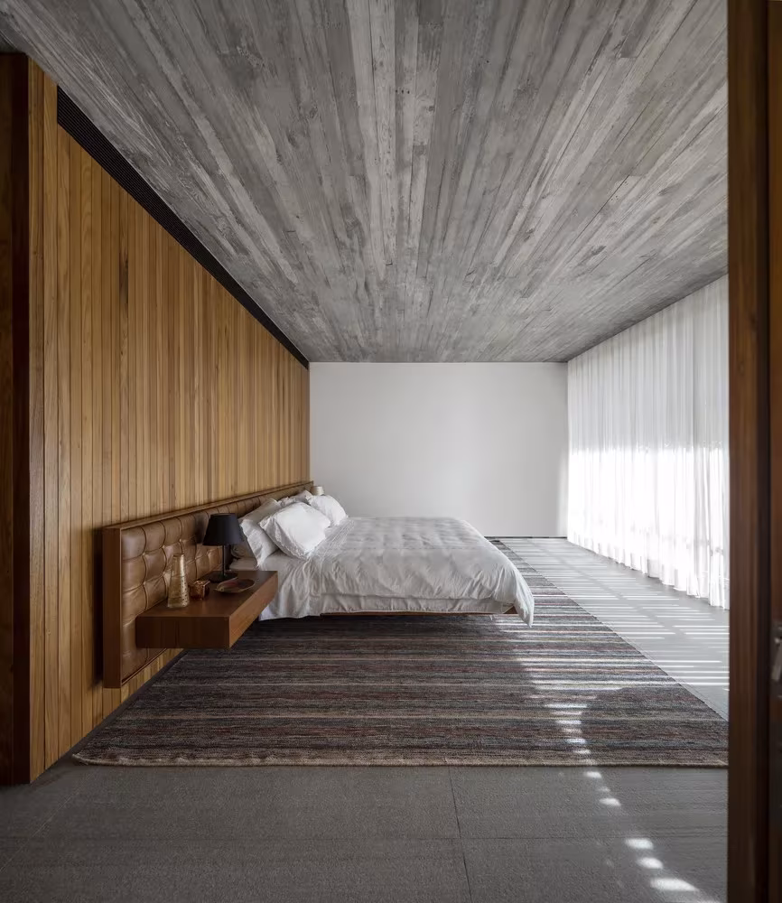 Dormitorio alargado de la Casa plana con panel de madera, cortinas blancas y alfombra de rayas, Marcio Kogan