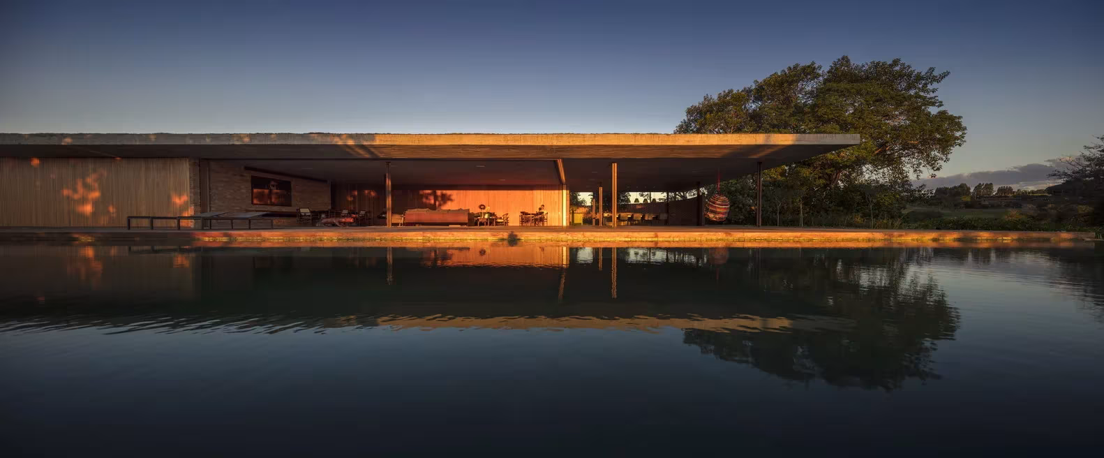 Losa horizontal de la Casa plana de Marcio Kogan sobre la lámina de agua y la luz cálida del interior, Porto Feliz