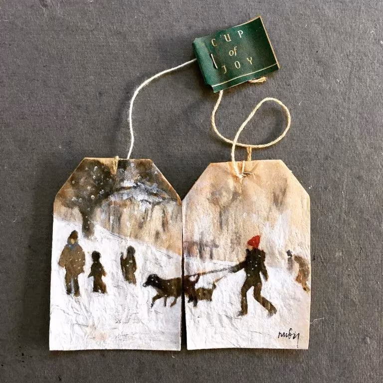 Dos bolsitas de té unidas pintadas por Ruby Silvious con una escena nevada de gente y un perro