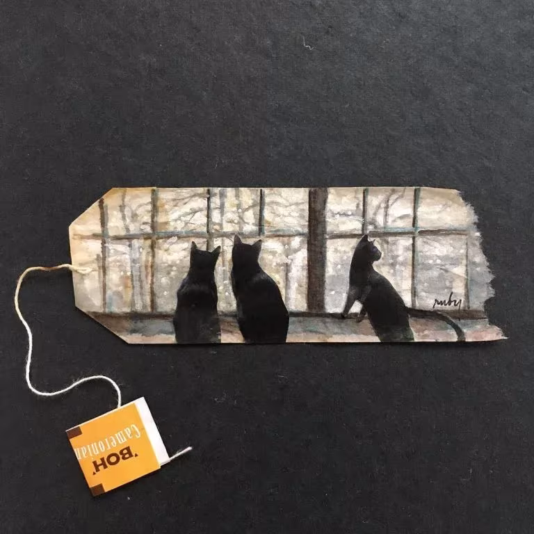 Bolsita de té pintada por Ruby Silvious con siluetas de tres gatos negros mirando por una ventana
