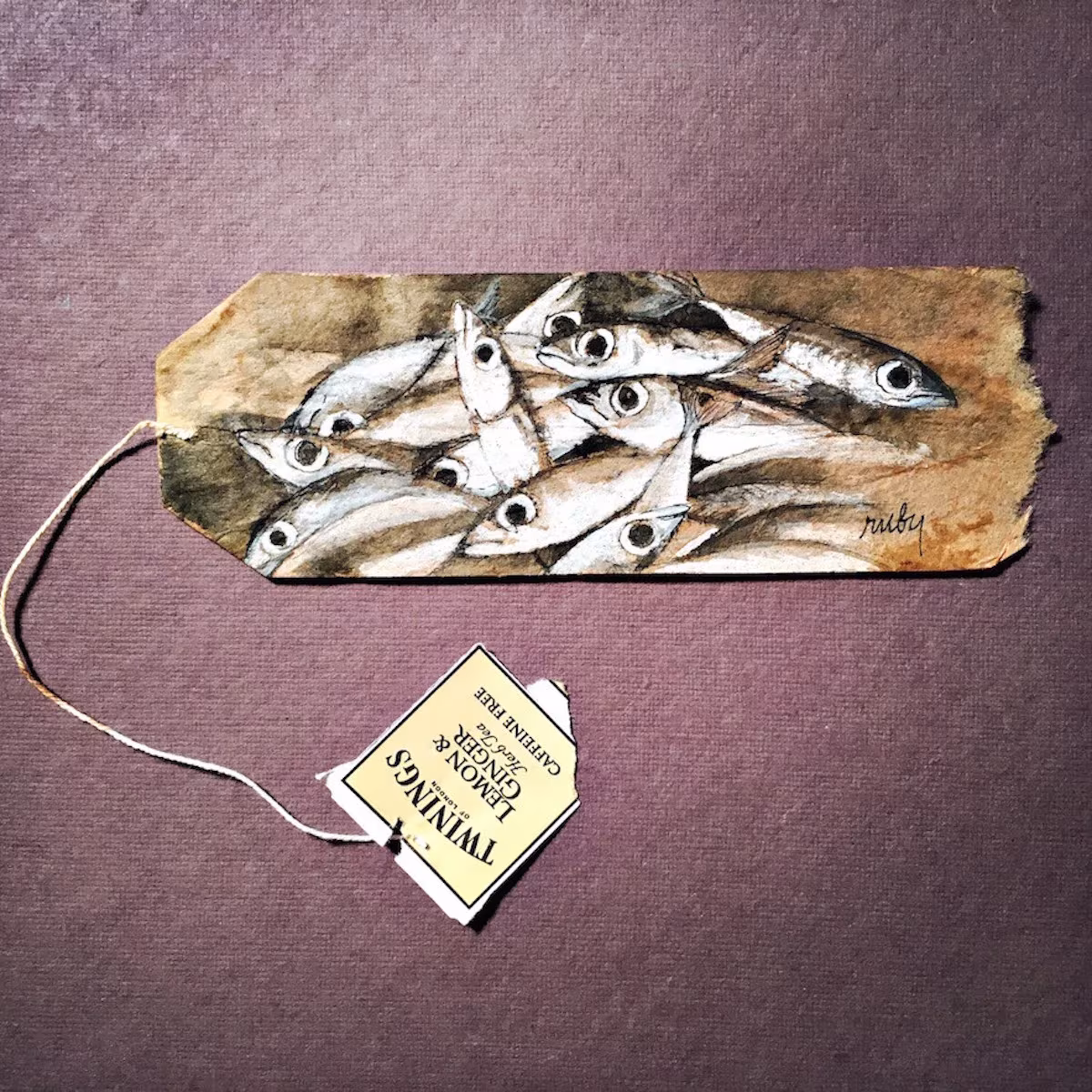 Bolsita de té pintada por Ruby Silvious con un banco de peces plateados sobre fondo morado