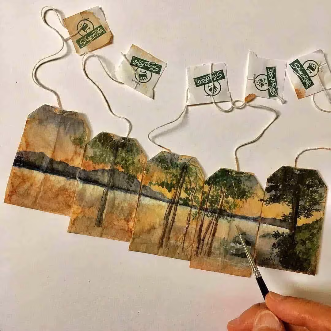 Mano pintando un paisaje de lago y árboles que se extiende por cinco bolsitas de té de Ruby Silvious