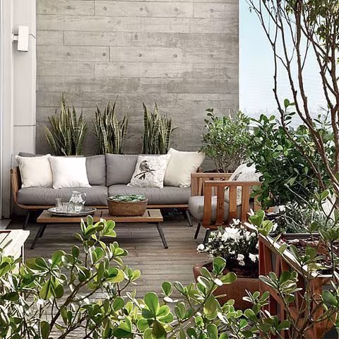 Terraza con sofá de exterior, cojines y plantas frente a un muro de hormigón con huella de encofrado