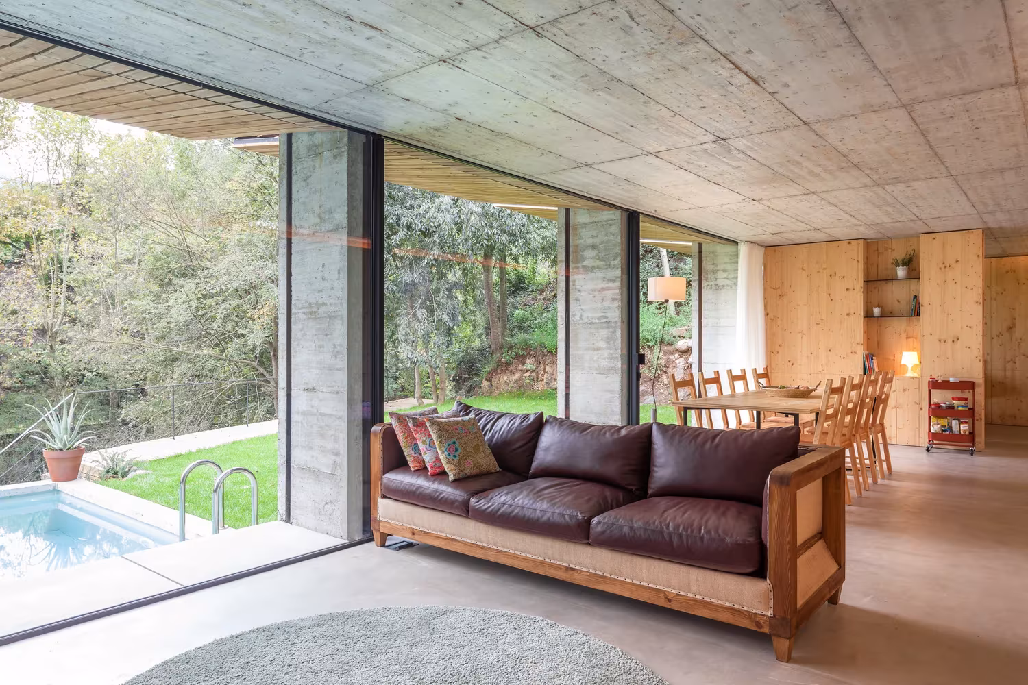 Salón con sofá de cuero y techo de hormigón abierto a la piscina en la Casa Retina de Arnau, Santa Pau