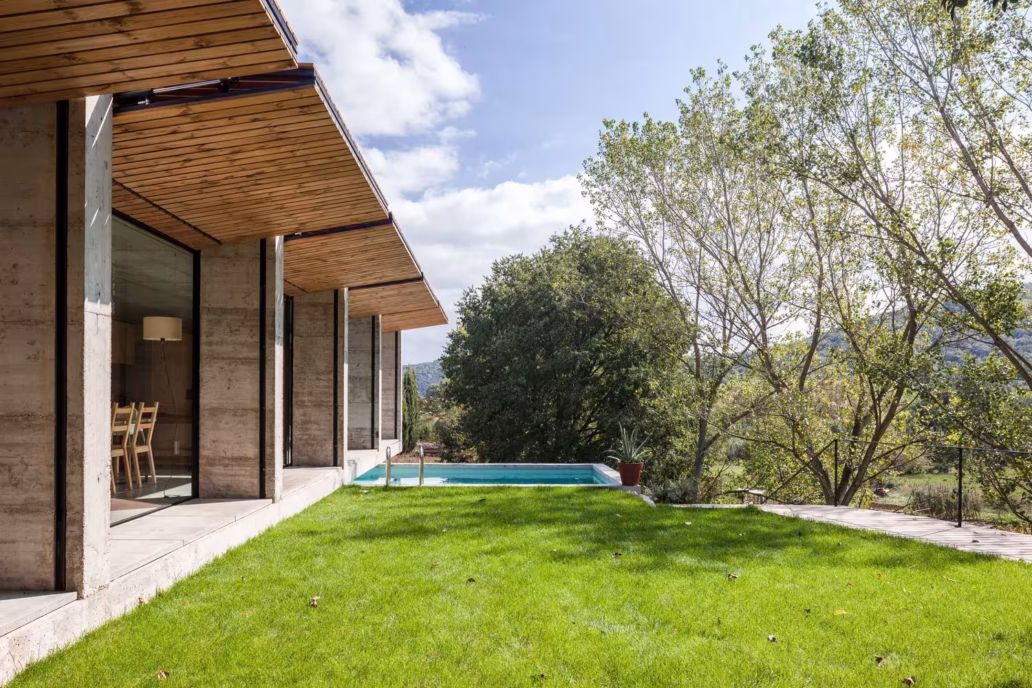 Voladizo de madera sobre el porche, césped y piscina de la Casa Retina de Arnau en Santa Pau