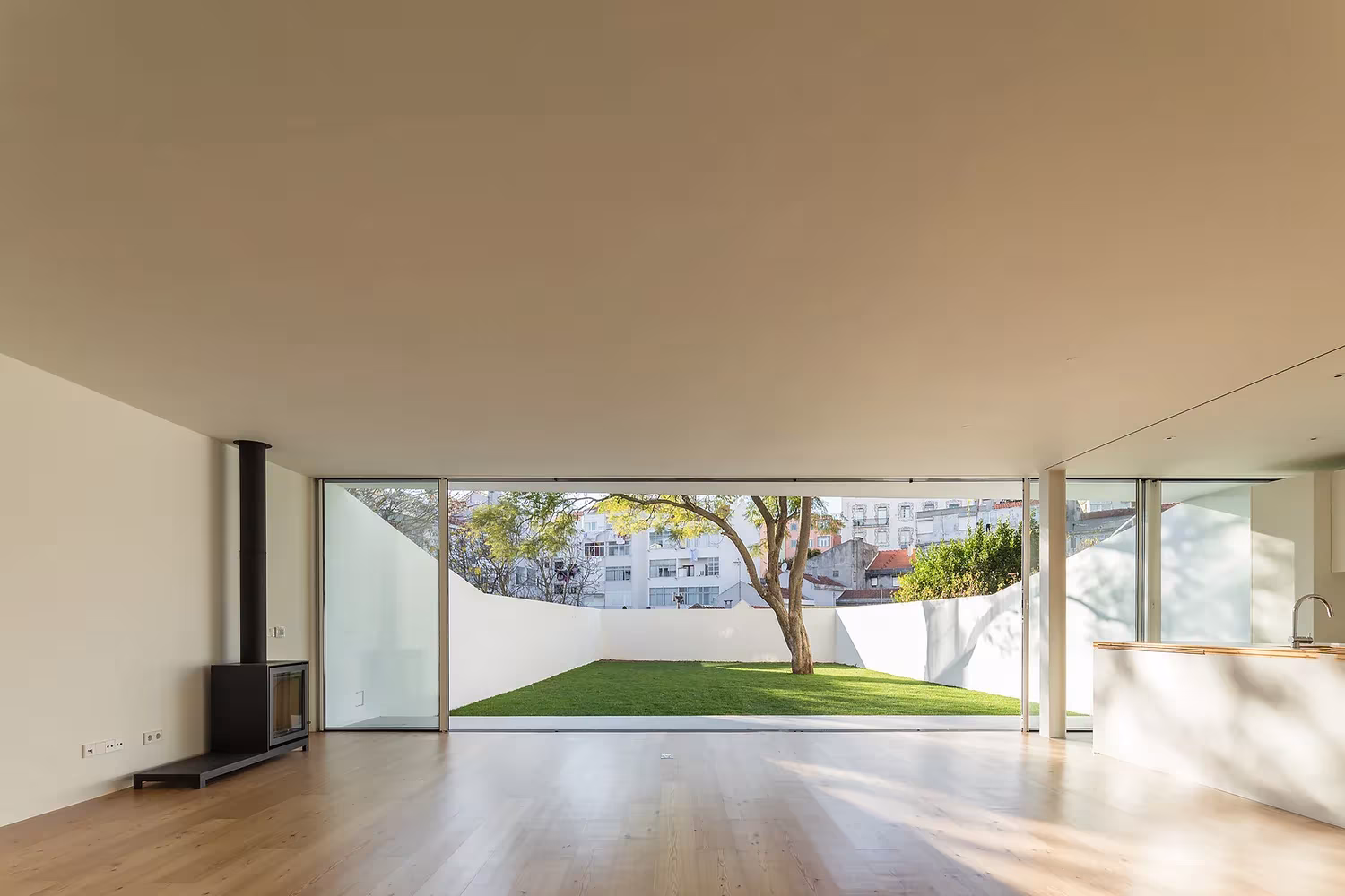 Salón con suelo de madera, estufa y gran ventanal corredizo hacia el jardín en la Casa Brotero de Lisboa
