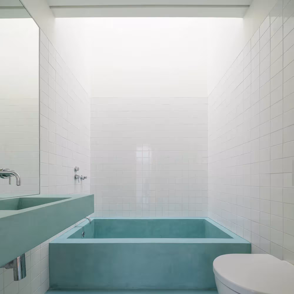 Baño revestido de azulejo blanco con bañera y lavabo de hormigón turquesa en la Casa Brotero, Lisboa