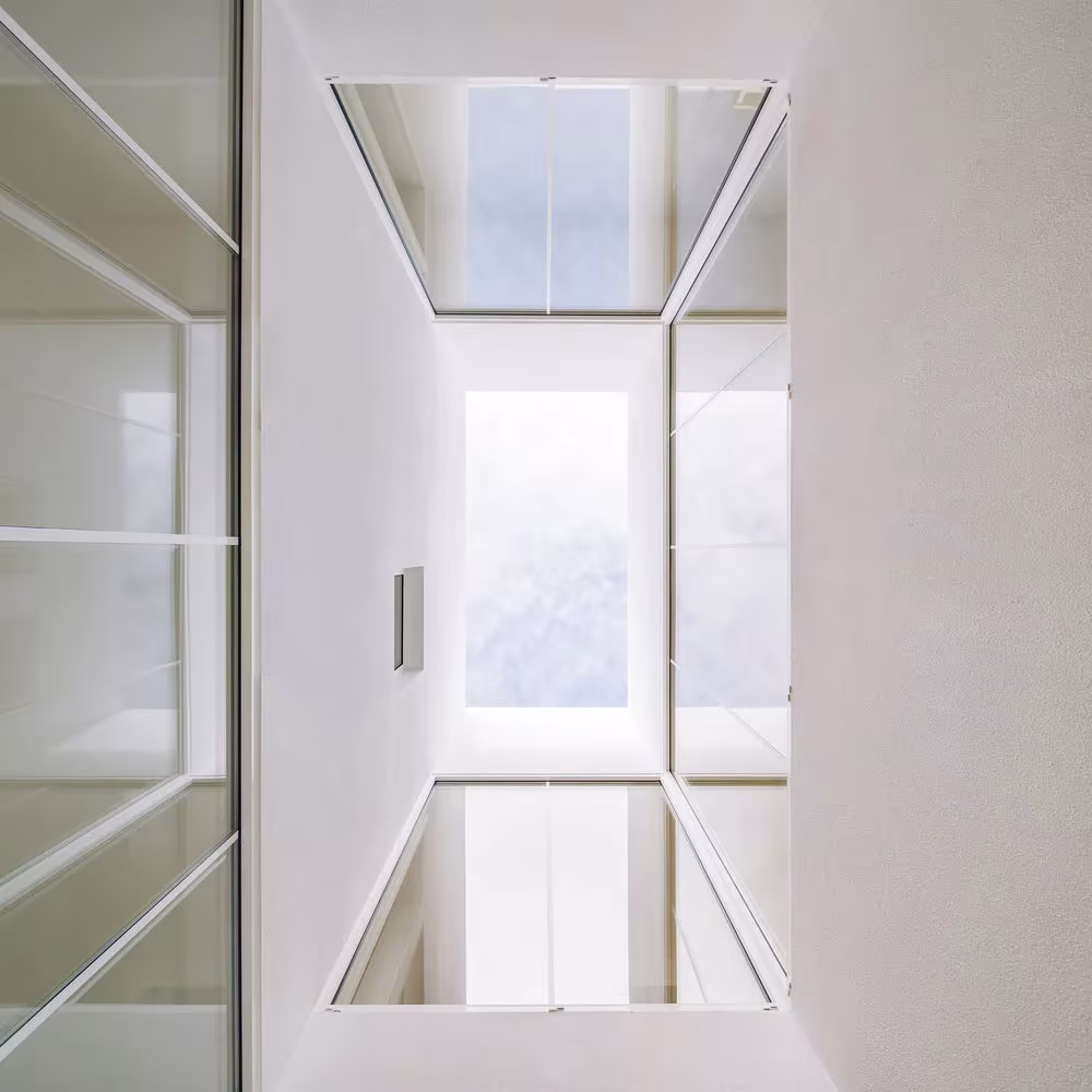 Vista cenital del patio interior de la Casa Brotero con paños de vidrio y cielo blanco, phdd arquitectos