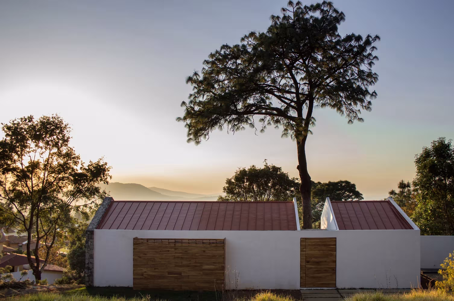 Casa de Espacio EMA con cubiertas rojizas partidas por un pino centenario en la sierra de Mazamitla, Jalisco