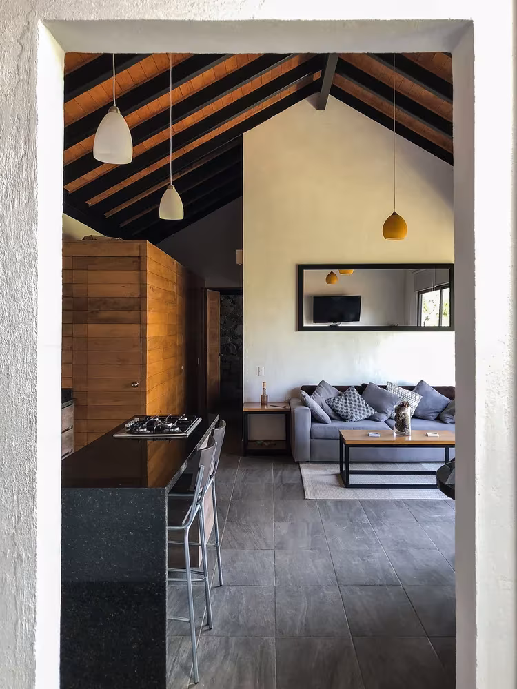 Salón y cocina bajo cubierta de madera vistos desde el umbral de la casa de Espacio EMA en Jalisco