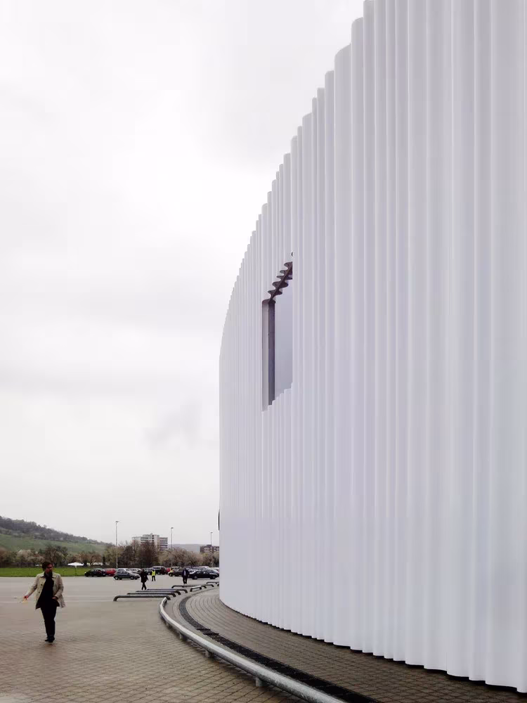 Peatón ante la fachada curva de chapa blanca del pabellón de SANAA para Vitrashop en el Vitra Campus