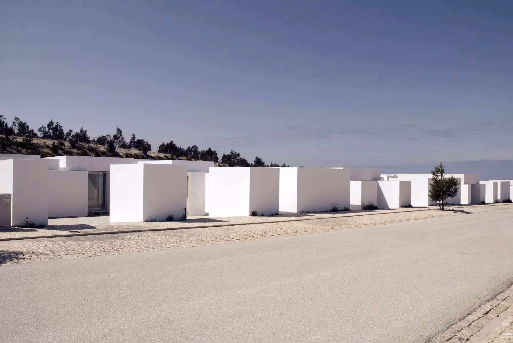 Calle de tierra bordeada por casas de volúmenes blancos en el complejo Quinta do Bom Sucesso, de Aires Mateus