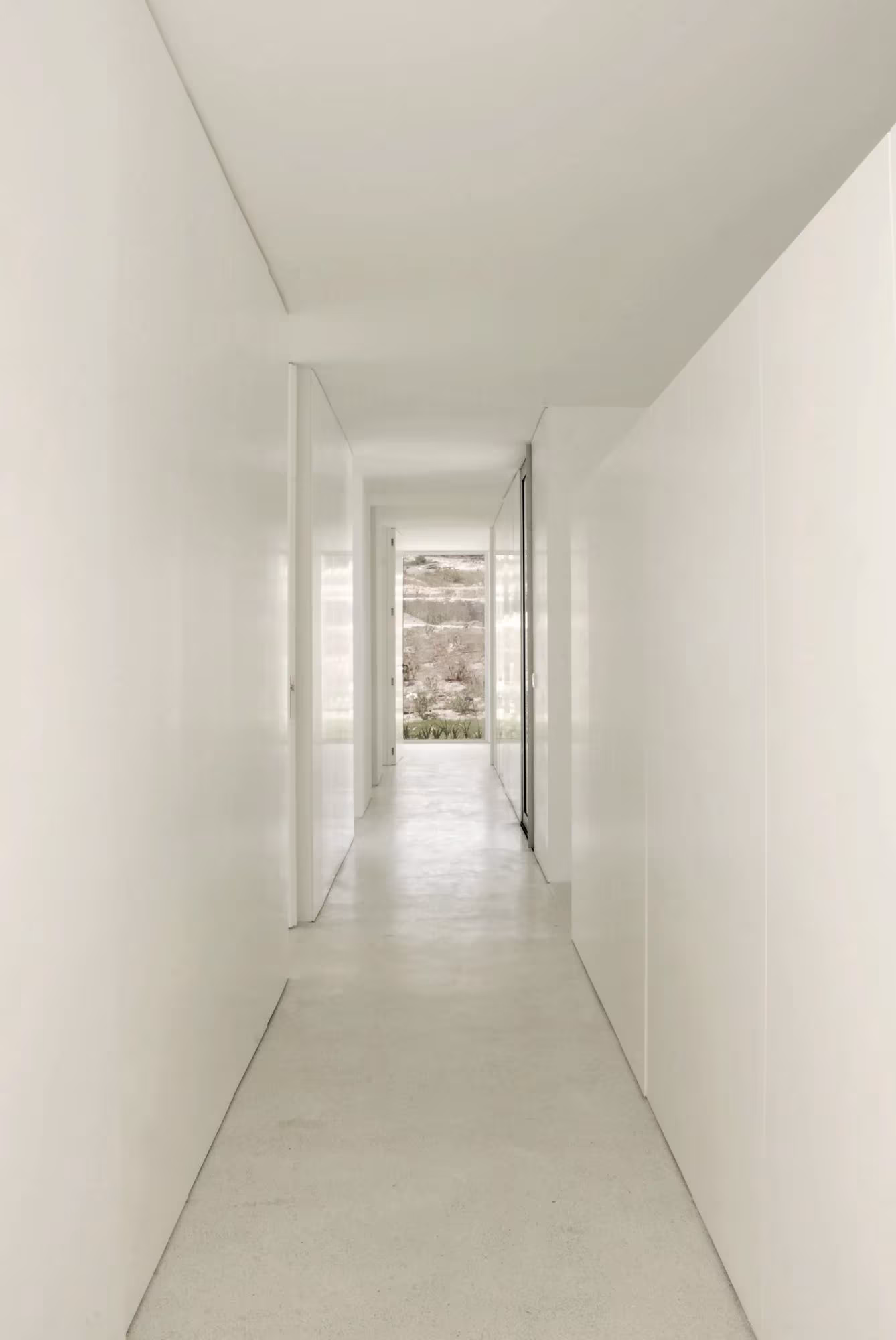 Pasillo largo de paredes blancas con luz natural al fondo en una vivienda de Quinta do Bom Sucesso