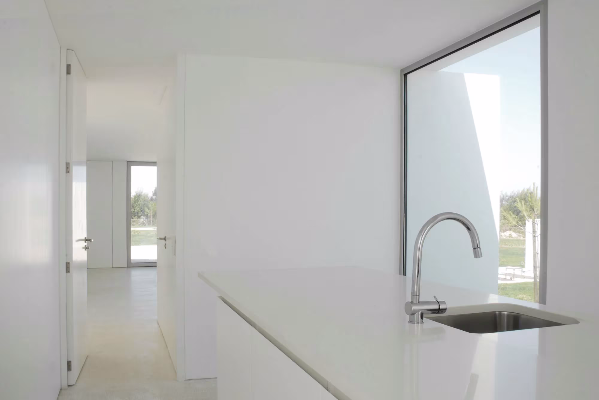 Cocina blanca con fregadero y ventanal de esquina abierto al paisaje en Quinta do Bom Sucesso, de Aires Mateus