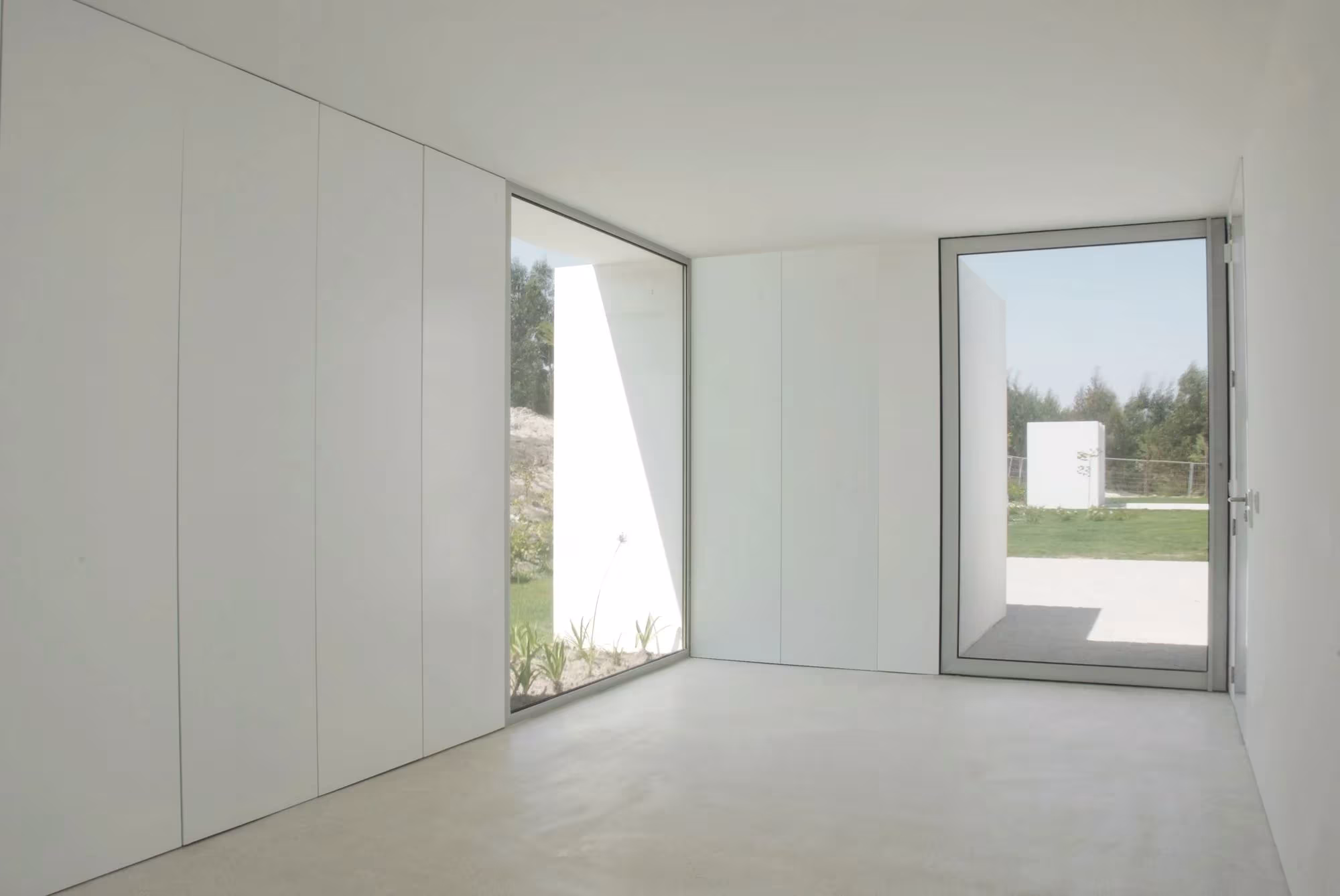 Salón blanco con armarios empotrados y gran ventana al jardín en una vivienda de Aires Mateus en Bom Sucesso