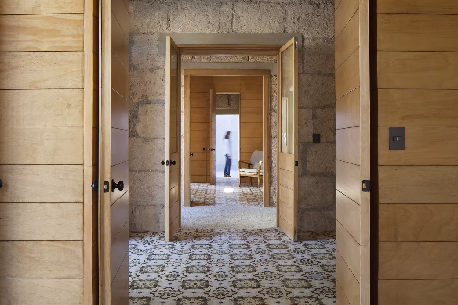 Enfilada de puertas de madera y muros de sillar sobre pavimento hidráulico en 15 de Mayo, de Oficio Taller