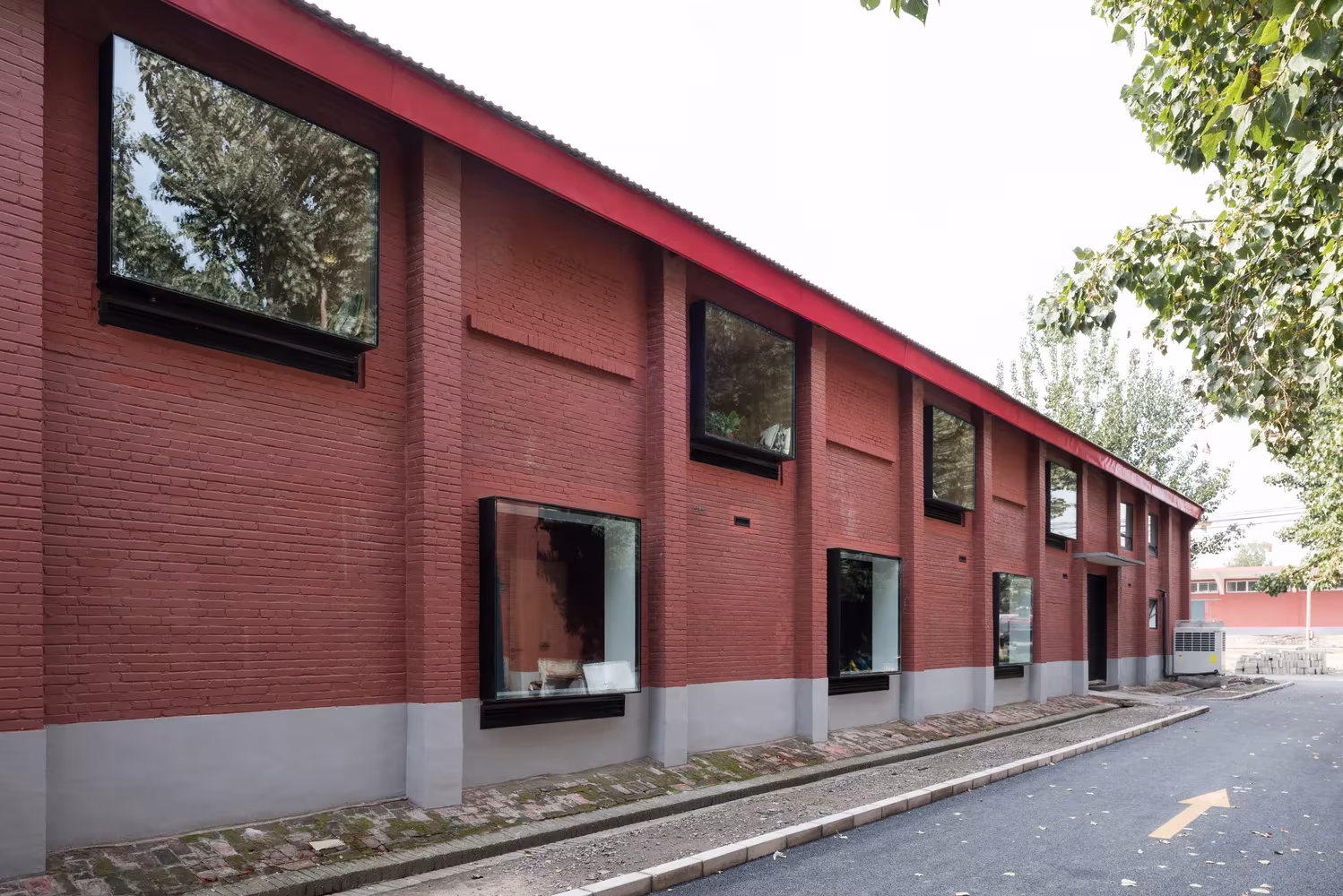 Fachada de ladrillo rojo del almacén de 1958 en Pekín con ventanas de marco negro y zócalo gris, sede de Lens Magazine