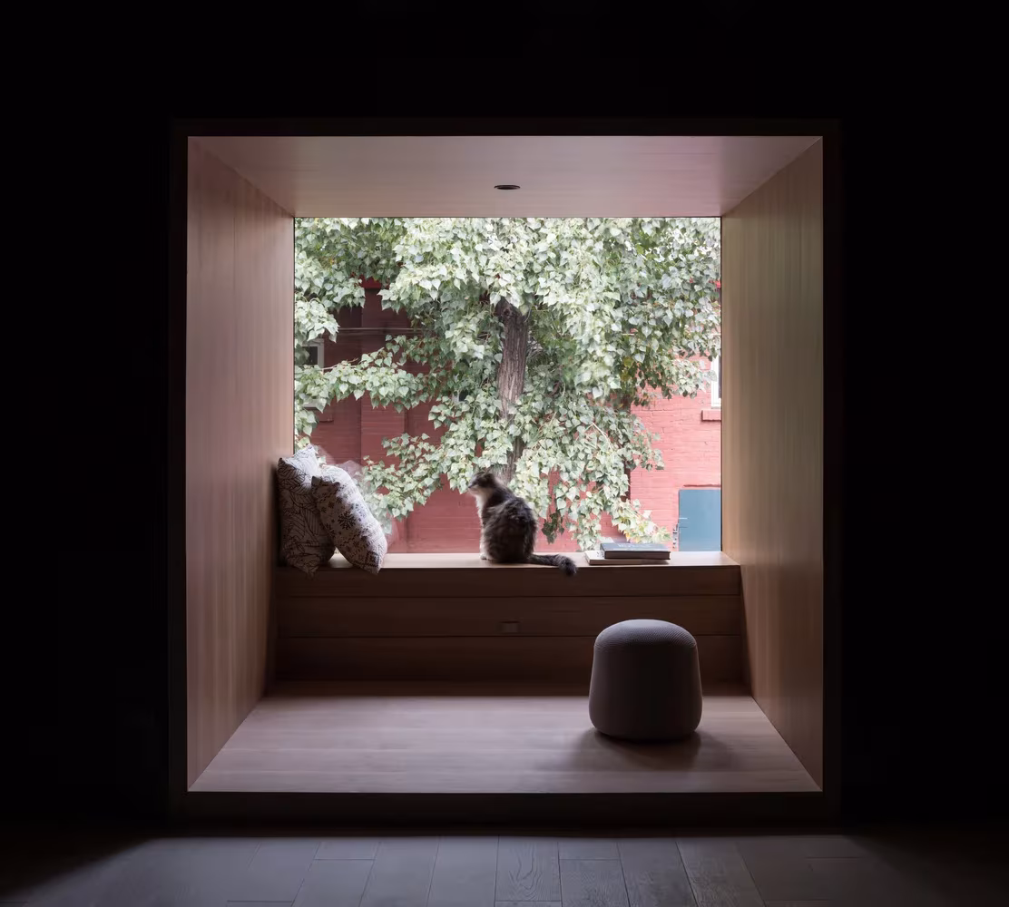 Mirador de madera clara enmarcado en negro con banco y puf frente a un árbol, en el almacén reformado por TAO en Pekín