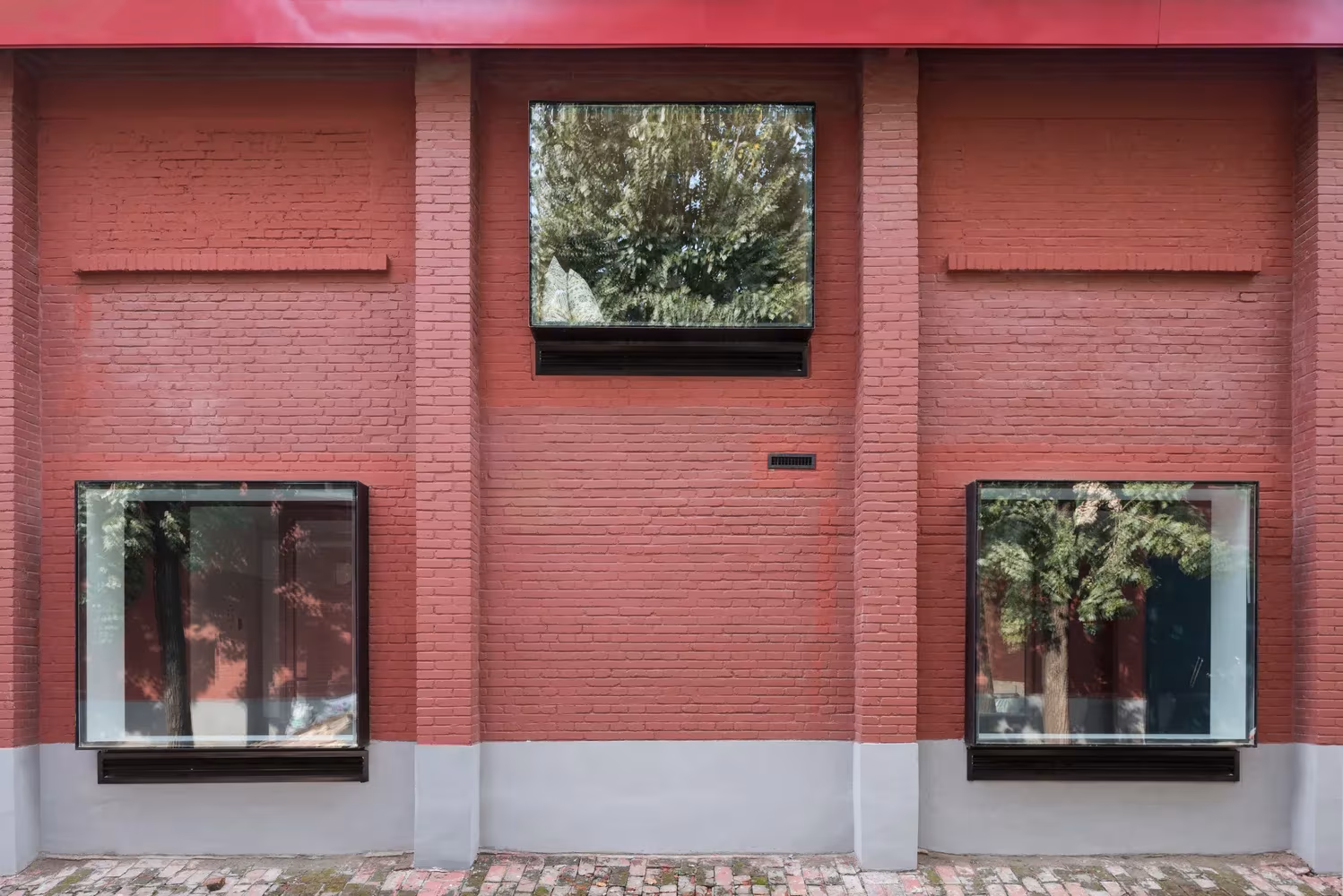 Detalle de la fachada de ladrillo rojo con dos ventanas de marco oscuro que reflejan los árboles, en Lens Magazine