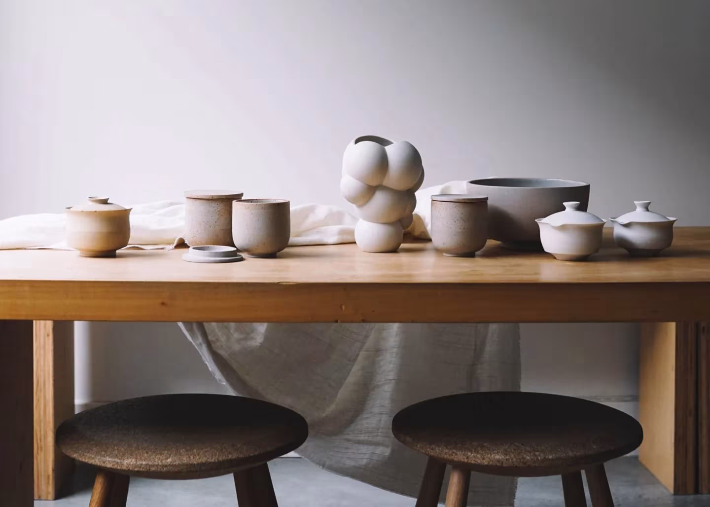 Jarrones SKUM de BIG y Mosss con formas hinchadas junto a cuencos de cerámica sobre una mesa de madera