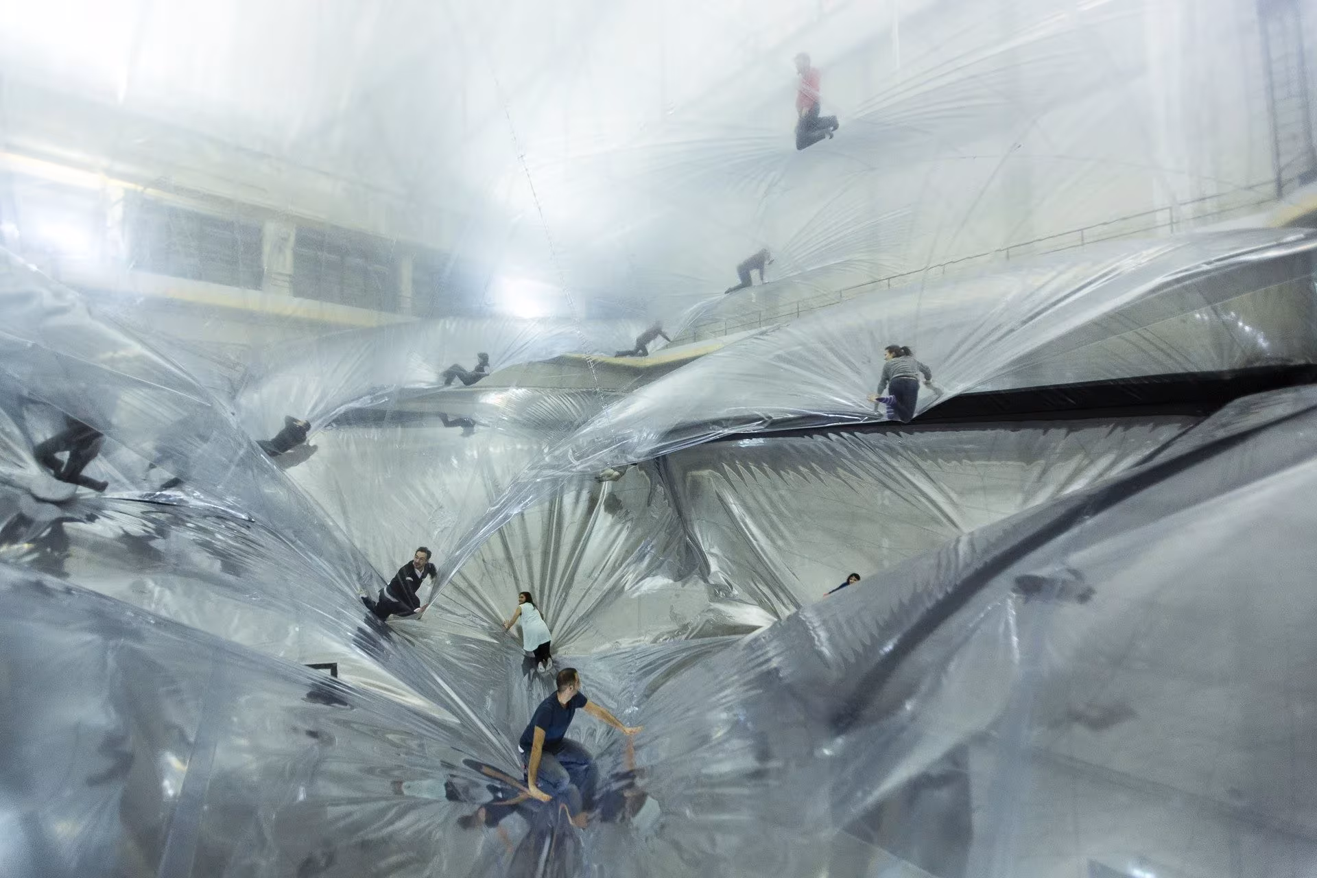 Visitantes trepando por las capas de plástico translúcido suspendidas de la instalación de Tomás Saraceno