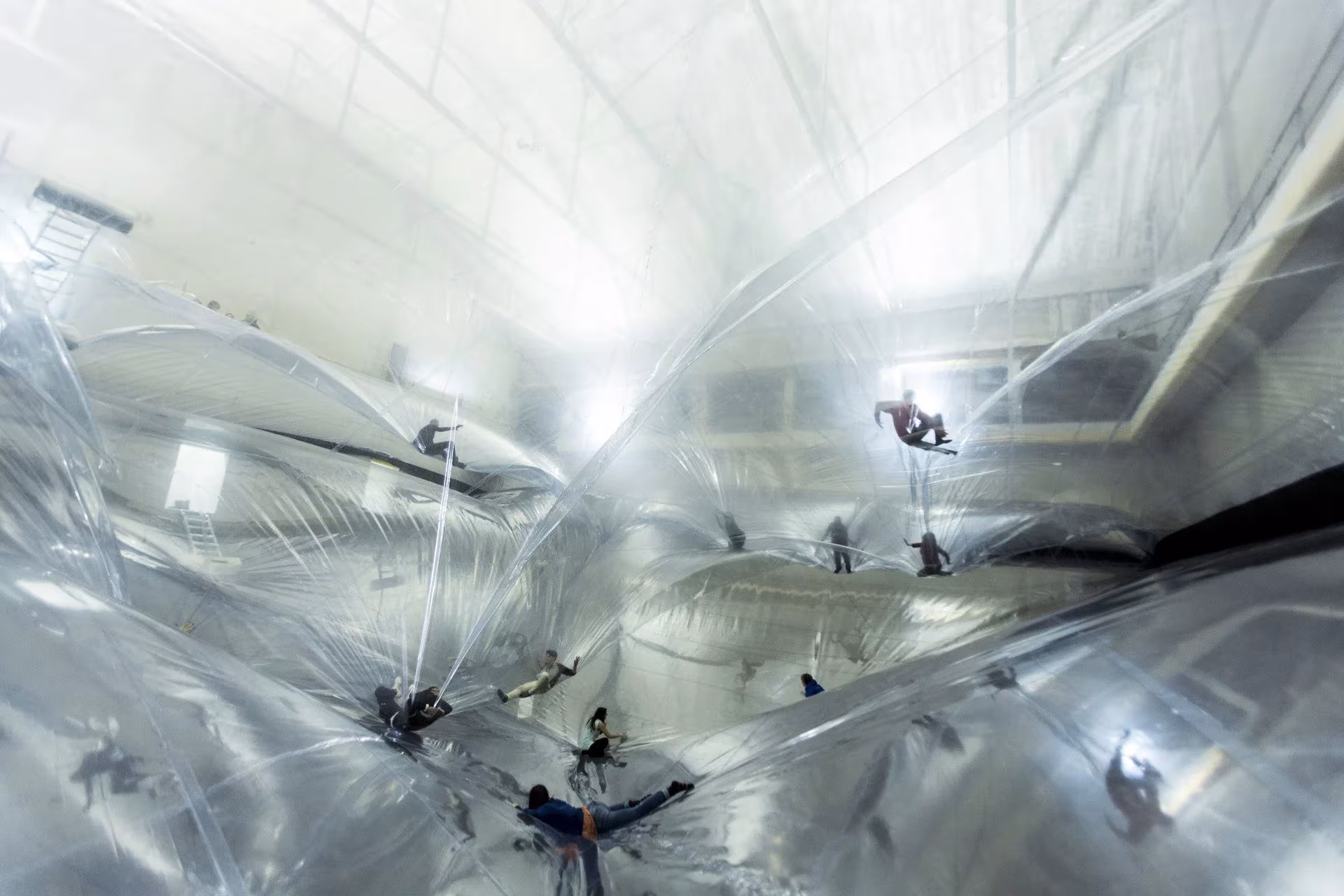 Vista desde abajo de On Space Time Foam de Tomás Saraceno, con siluetas de personas sobre la membrana brillante