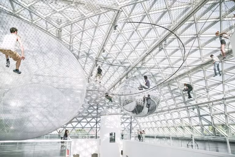 In Orbit de Tomás Saraceno, red de acero con esferas de aire y personas suspendidas bajo una cúpula de vidrio