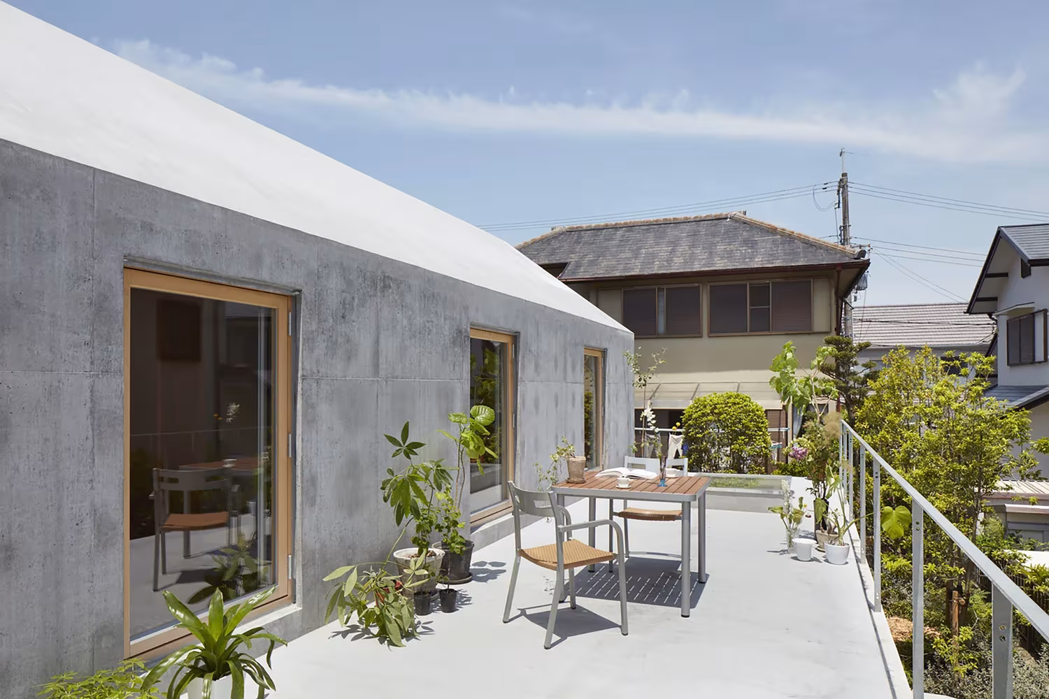 Terraza de hormigón con mesa y plantas junto al muro con ventana de madera en la casa de Tomohiro Hata en Otsu