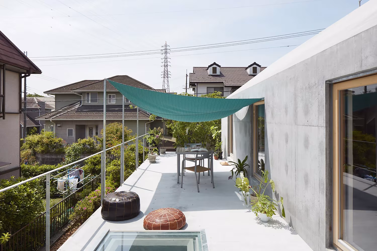 Terraza con toldo verde, lucernario en el suelo y muro de hormigón con vistas al barrio, en la casa de Tomohiro Hata