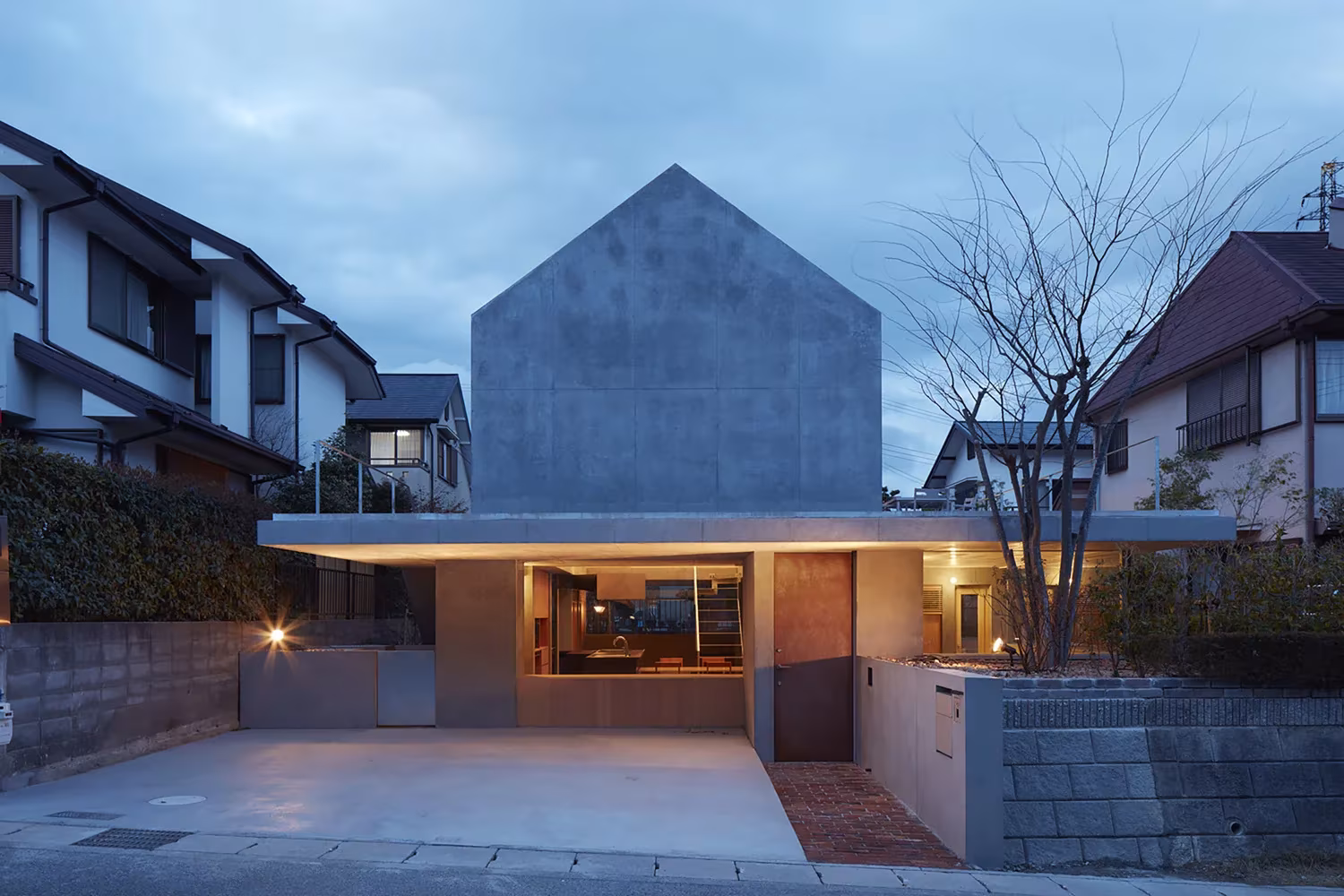 Frontón de hormigón sobre el porche de acceso entre casas vecinas de Otsu al anochecer, de Tomohiro Hata Architects