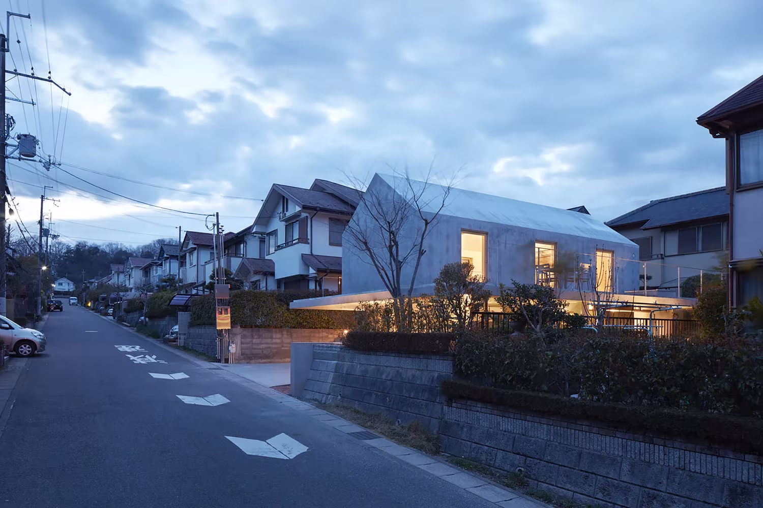 Calle residencial de Otsu con la casa de hormigón de Tomohiro Hata entre las viviendas vecinas al anochecer