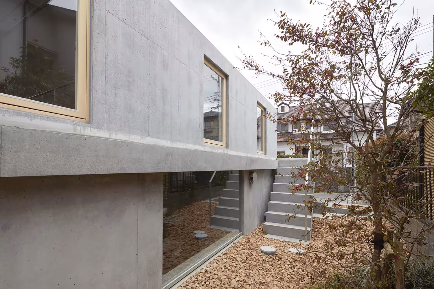 Volumen de hormigón con ventana de madera sobre la planta baja acristalada y escalera exterior, de Tomohiro Hata