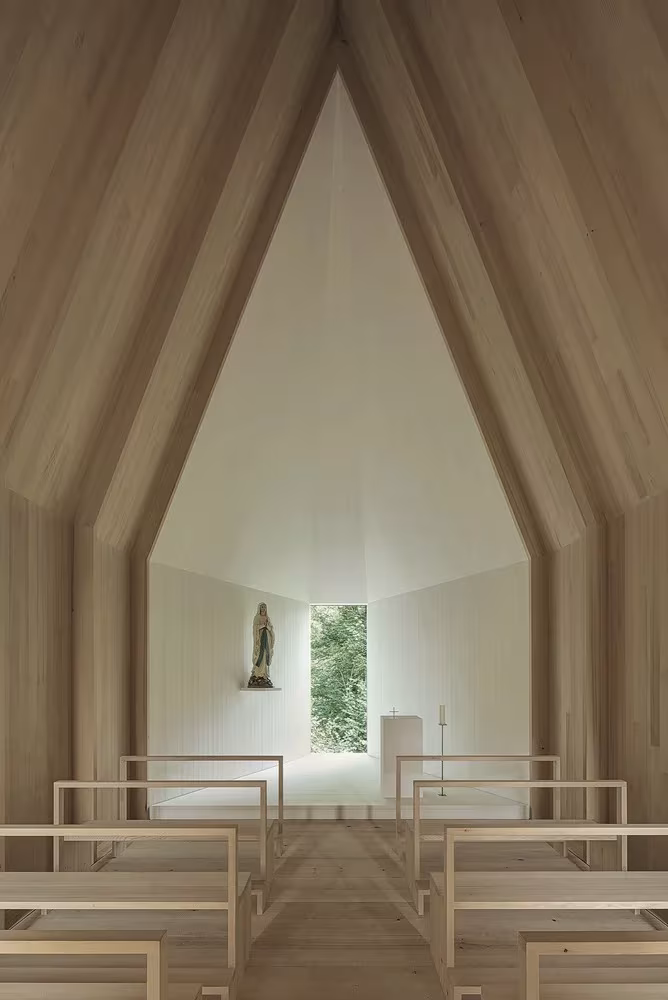 Interior de la Capilla Salgenreute con nervios de madera apuntados, bancos corridos y ventana al fondo