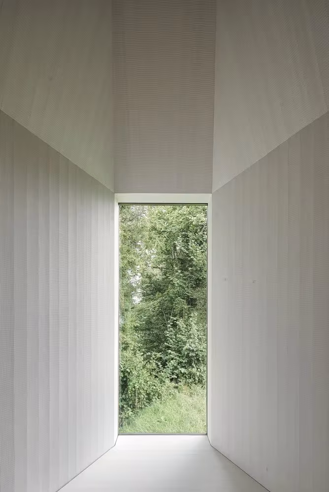 Interior blanco de la capilla con un vano alto que enmarca el bosque, de Bernardo Bader en Krumbach