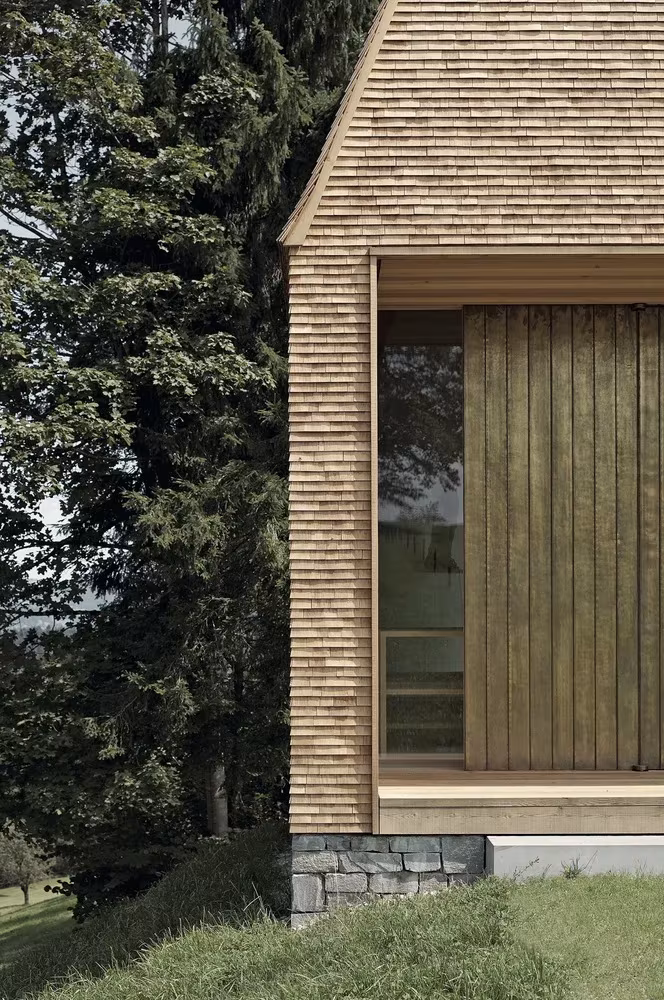 Esquina de la Capilla Salgenreute con tejuelas de madera, ventana y tablas verticales junto a los abetos