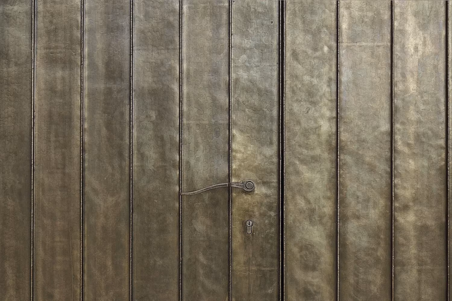 Detalle de la puerta de latón con tirador sobre paneles verticales de la Capilla Salgenreute