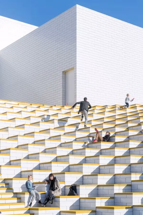 Escalinata blanca de la plaza elevada de la LEGO House, de BIG, con visitantes sentados junto al volumen blanco