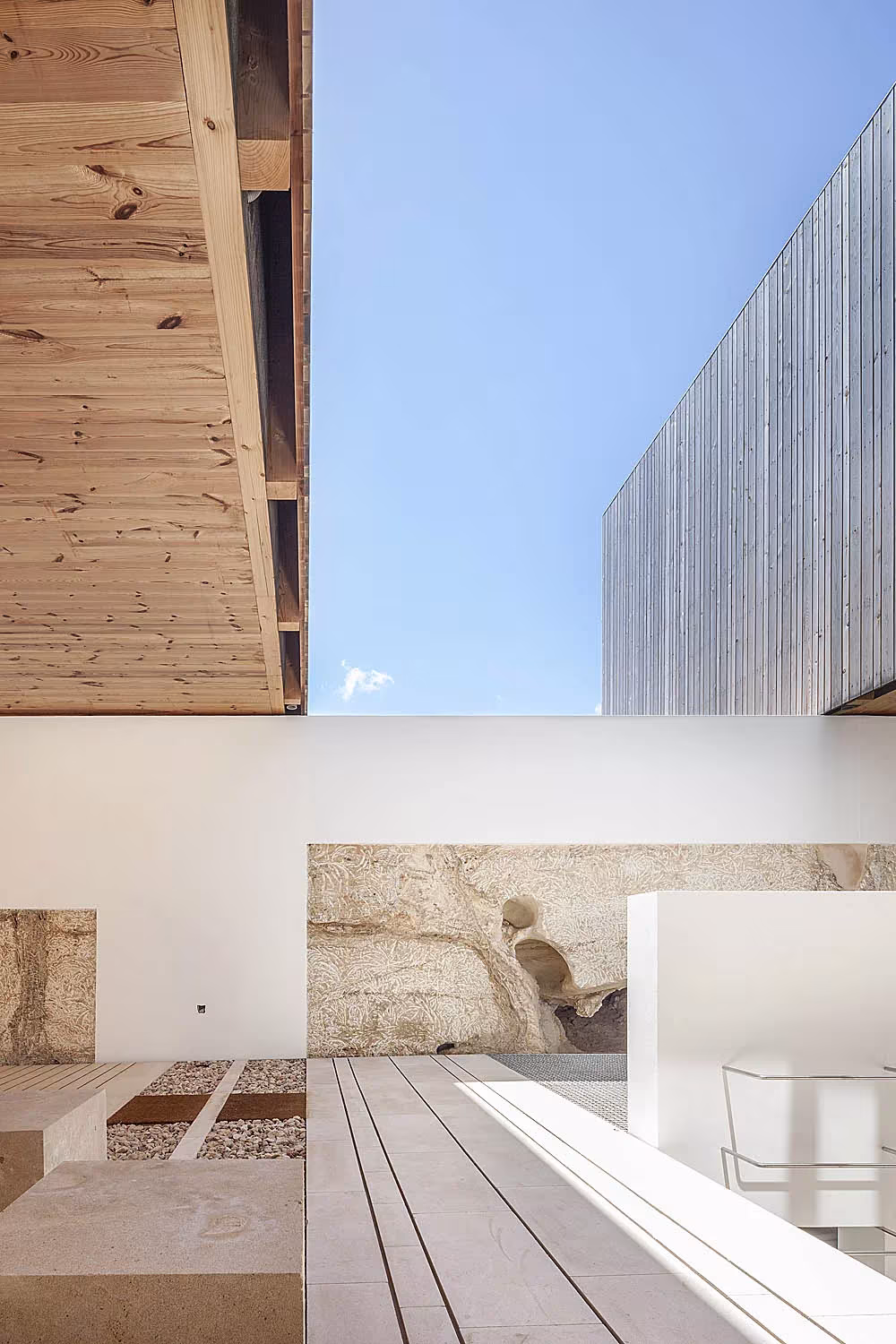 Patio blanco con suelo de madera y bancos de piedra bajo el voladizo de madera de Bosc d'en Pep Ferrer