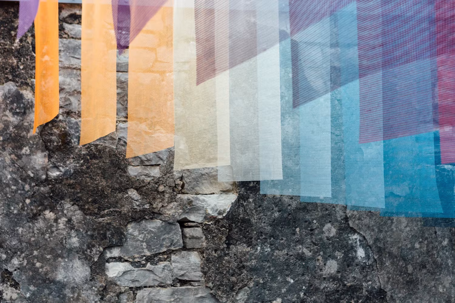 Telas translúcidas de colores colgadas sobre un muro de piedra en el edificio en ruinas de Paxos, instalación de Quintessenz