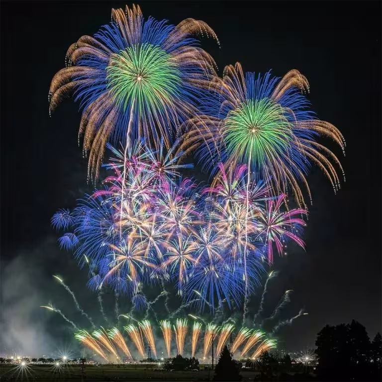 Fuegos artificiales de colores en un festival de hanabi japonés, con estallidos azules y verdes sobre el campo nocturno