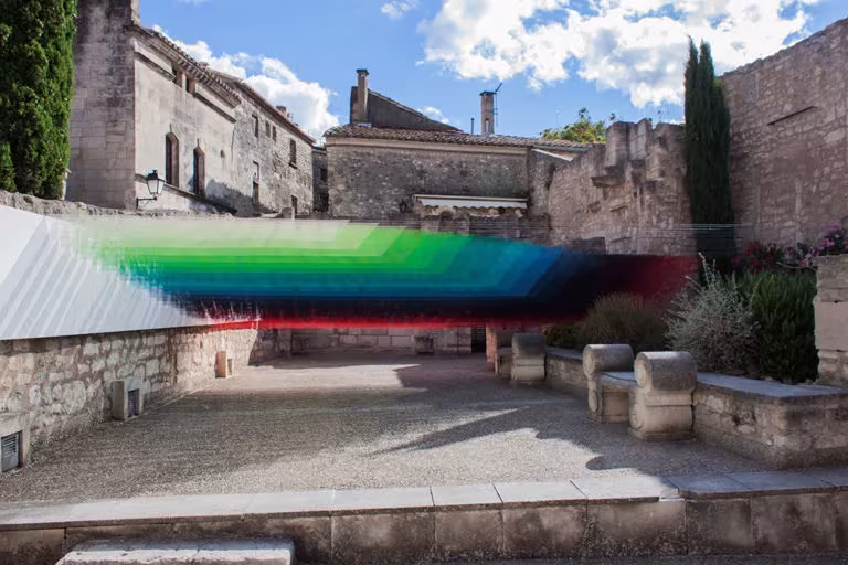 Instalación de Quintessenz con franjas de colores verde, azul y rojo tendidas sobre un patio de piedra en ruinas